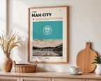 Poster minimaliste encadré de Manchester City accroché au mur dans un salon lumineux et bien visible, design premium bleu ciel.