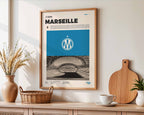Poster minimaliste encadré de l'Olympique de Marseille accroché au mur dans un salon lumineux et bien visible, design premium bleu ciel.