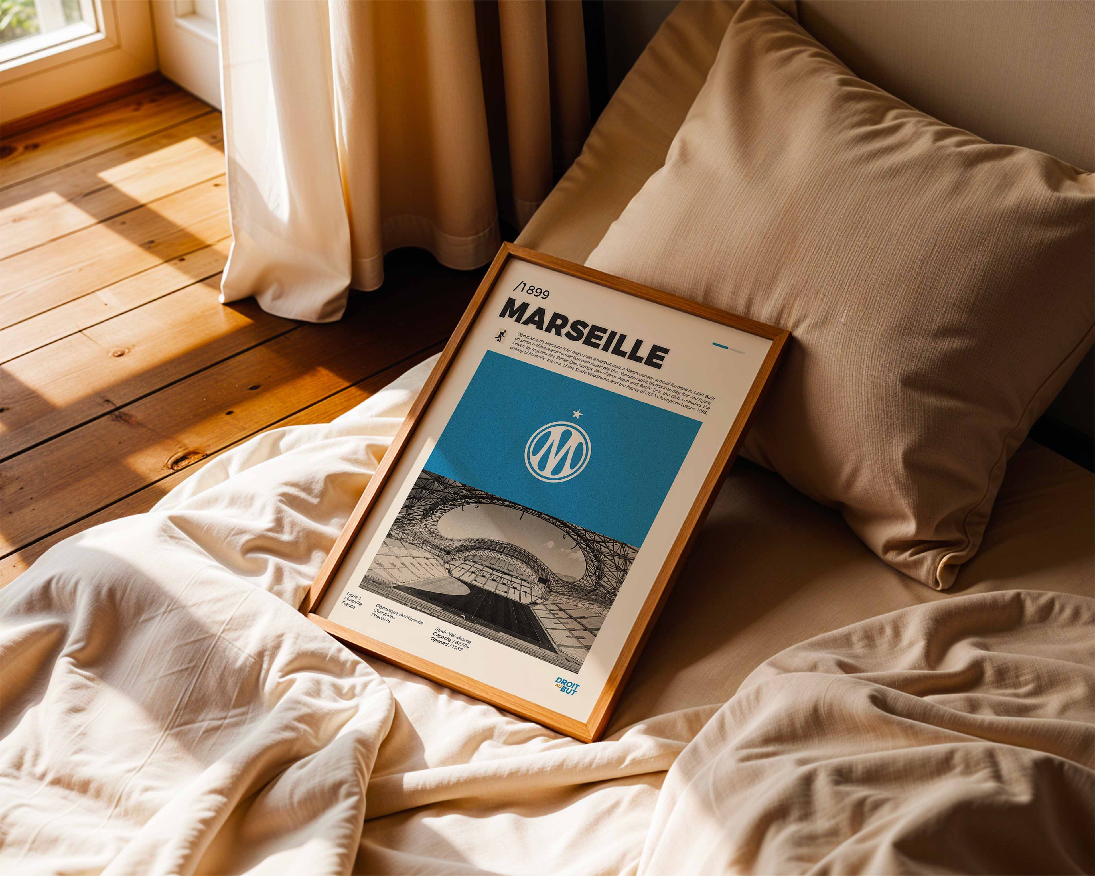 Poster minimaliste encadré de l'OM posé sur un lit dans une chambre, idée cadeau fan de football Marseille.