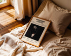 Poster minimaliste encadré de Werenoi Pyramide posé sur un lit dans une chambre, idée cadeau fan du Carré.